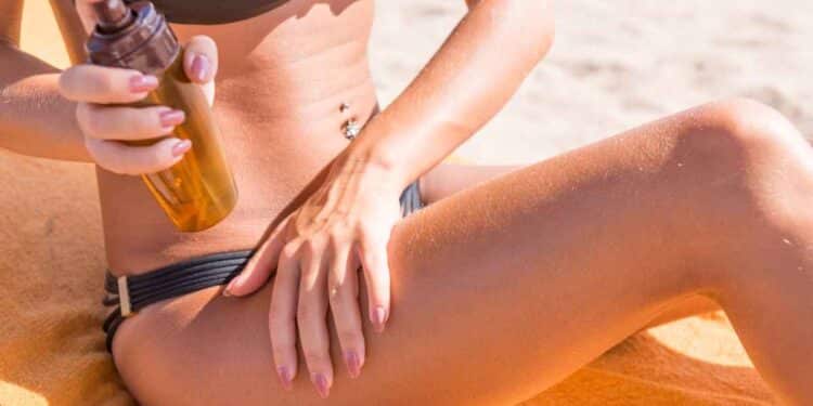 Sensuous slim woman applying suntan lotion oil to her body at the beach